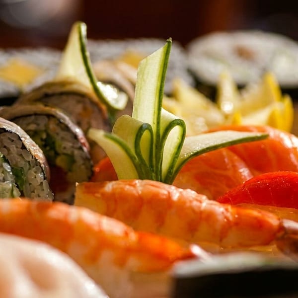 Close-up platter of assorted sushi rolls, shrimp, salmon, tuna, and decorative cucumber garnish.
